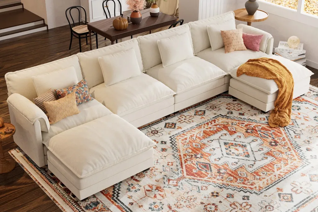 An off-white L-shaped modular sectional sofa with various cushions and a burnt orange patterned rug.