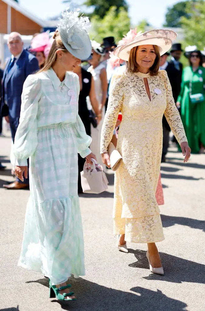 Alizée in a green hat and dress walking next to Carole Middleton in yellow