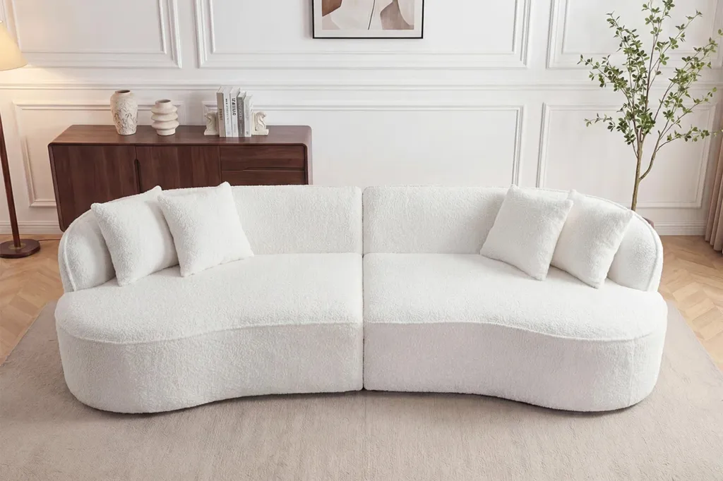Two-piece white curved sofa with white pillows.