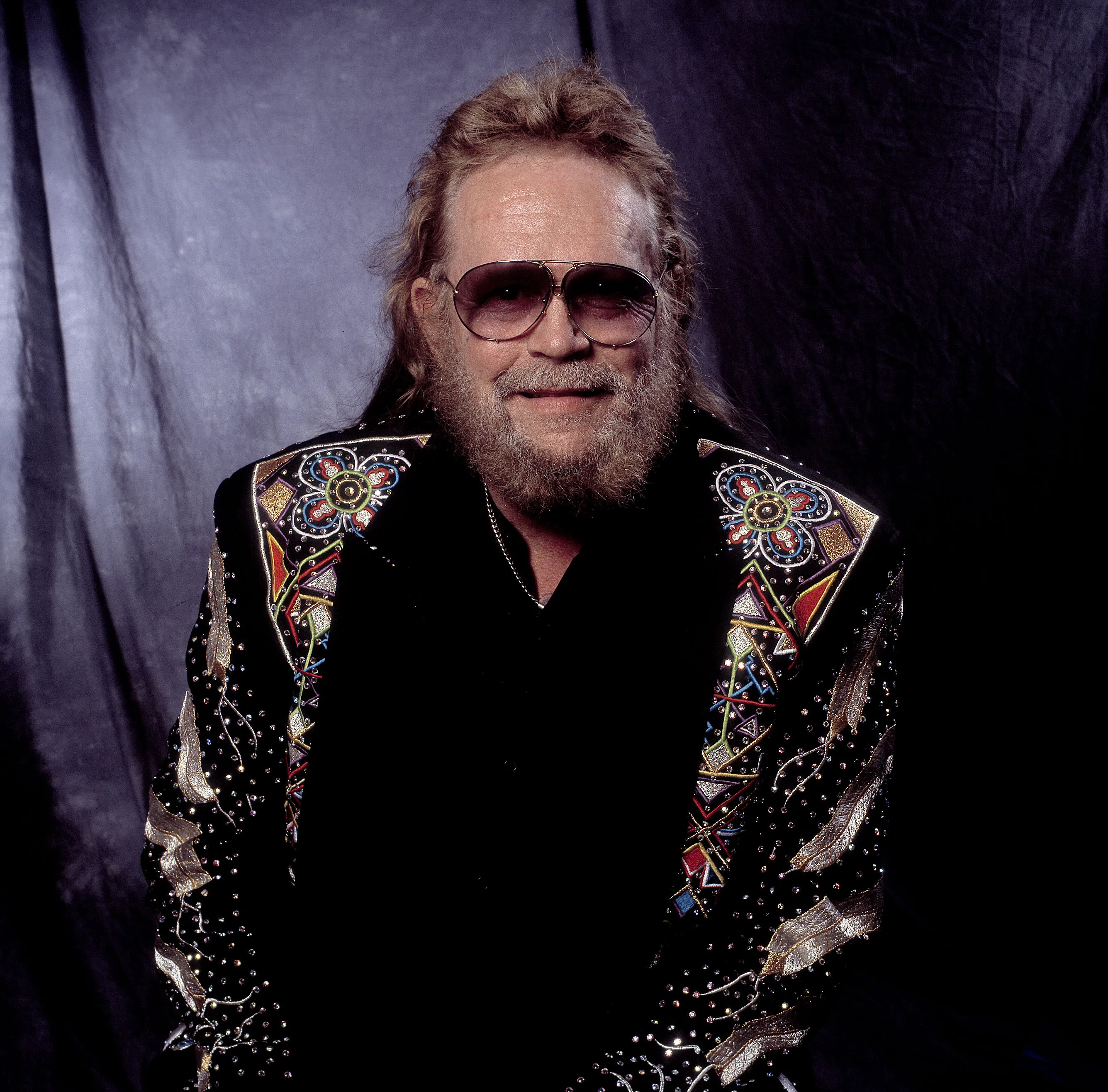 Country music singer David Allan Coe in a black suit with colorful embroidery and sunglasses.