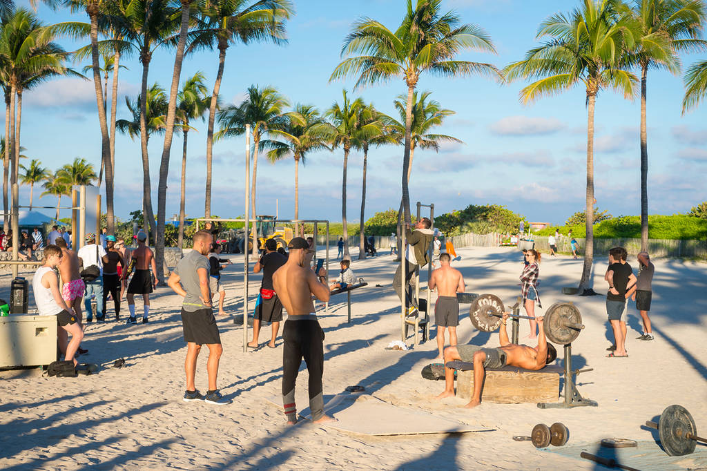 MIAMI - DECEMBER 27, 2017: Muscular young men exercise at the outdoor fitness resort known locally as Muscle Beach South Beach, which attracts passers-by passing by the Lummus Park boardwalk.
