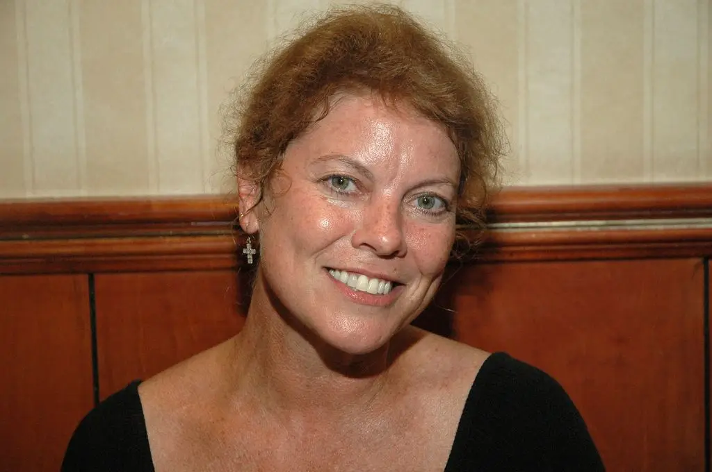 Erin Moran in a black top, sitting against a half-paneled wall.