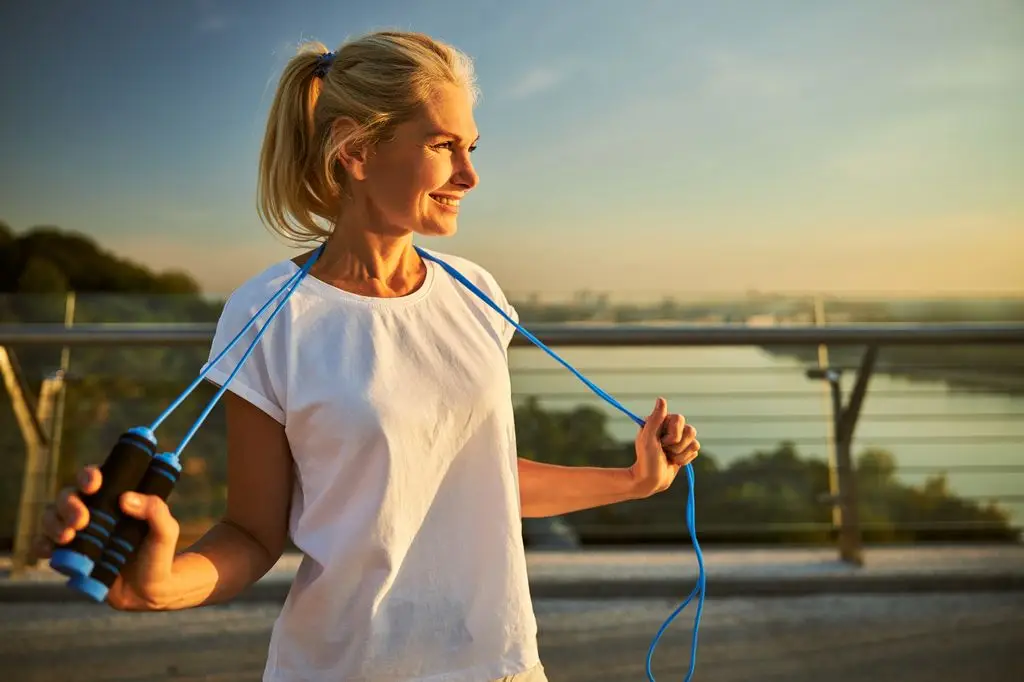 A woman in a white t-shirt smiles while holding blue resistance bands.
