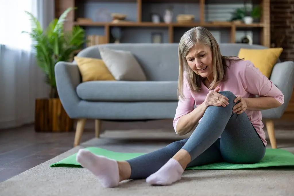 5 each day habits to hurry up your joint ache 1 A woman in a pink shirt and gray leggings sits on a yoga mat, holding her knee.