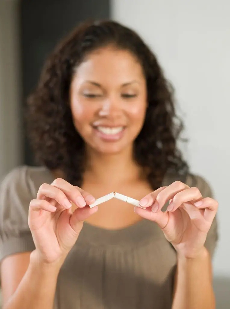 A woman with curly hair is holding two broken cigarettes, smiling.