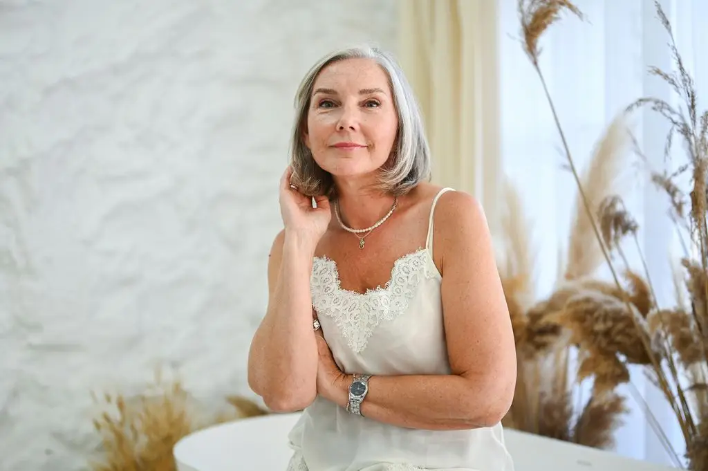 Mature woman with gray hair looking at camera, wearing camisole and pearl necklace
