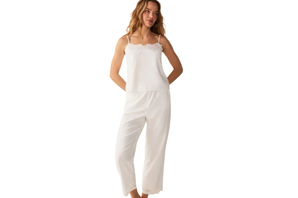 A woman wearing white pajama pants and a white camisole decorated with lace.