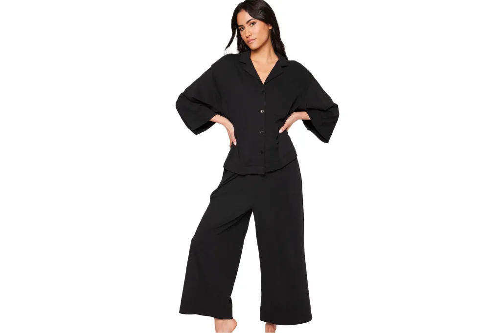 Dark-haired woman posing in a black button-down top and matching wide-leg pants.