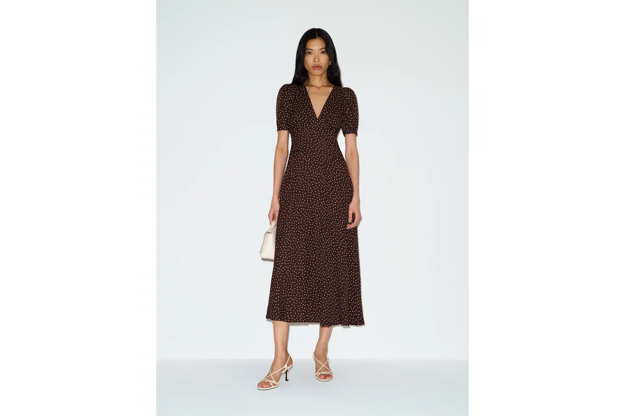 Woman wearing brown polka dot midi dress and white strappy heels.