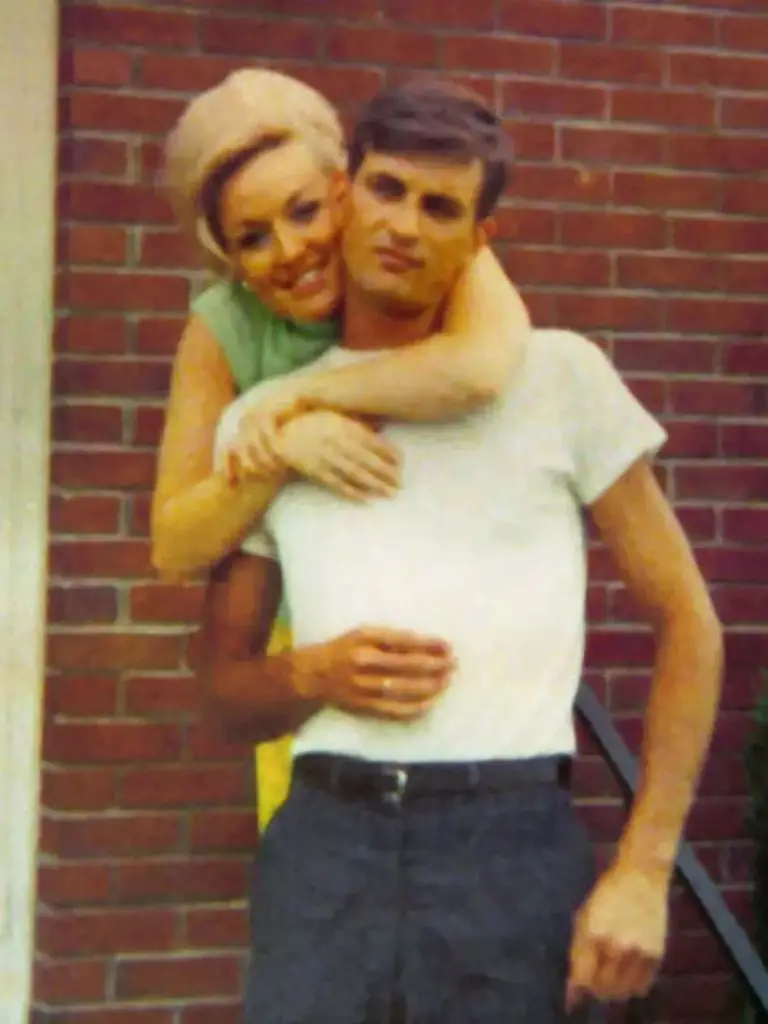 a young Dolly Parton standing behind Carl Dean with her arms around his neck