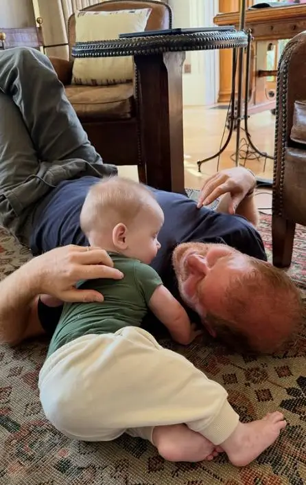 Man lying on a rug with baby on his chest, both looking at something.