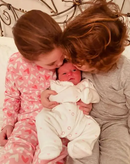 Meet Strictly star Lacey Turner's 3 children she shares along with her husband after tragic miscarriages 2 Two young children in pajamas kiss a swaddled baby, showing affection.