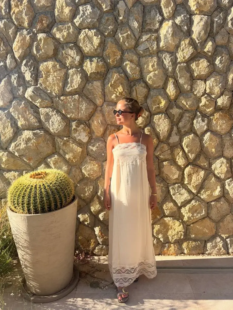 Duke of Kent's granddaughter Girl Amelia Windsor stuns in gorgeous Spanish bikini photographs 2 A woman in a white dress stands near a stone wall and wears sunglasses.
