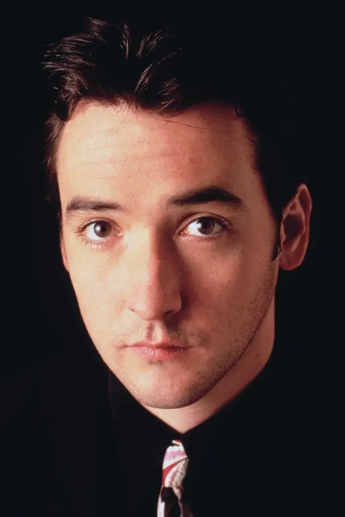 Photo of John Cusack wearing a dark shirt and colorful tie.