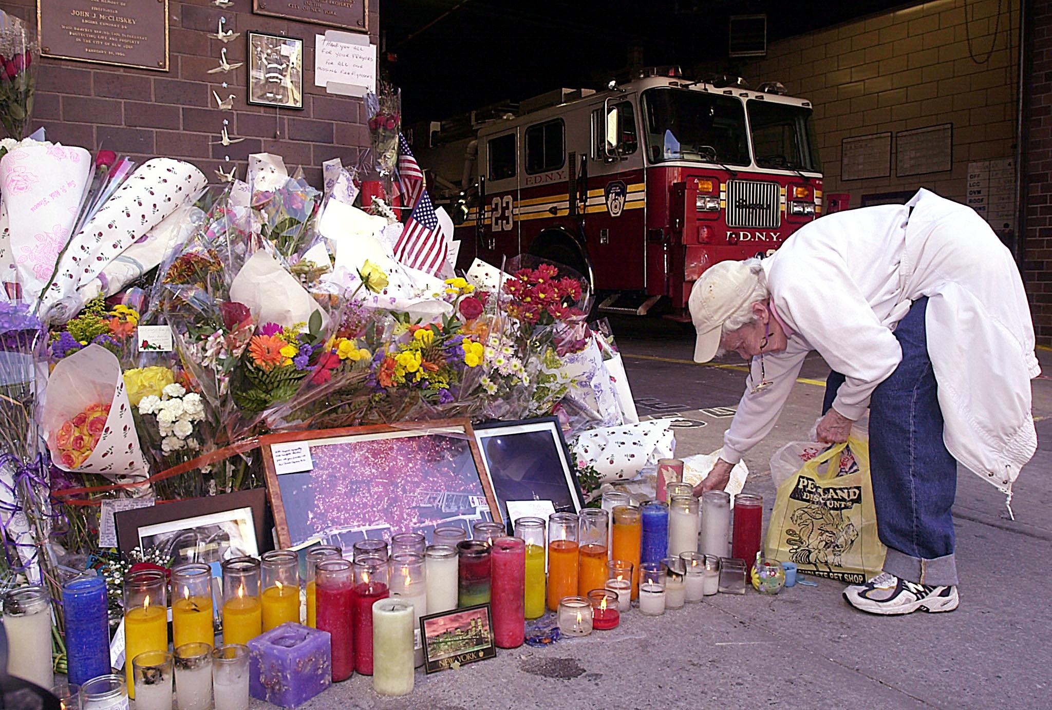 A woman lights a candle at a memorial for the victims at a Manhattan fire station, September 13, 2001. (Photo by TANNEN MAURY/AFP via Getty Images)
