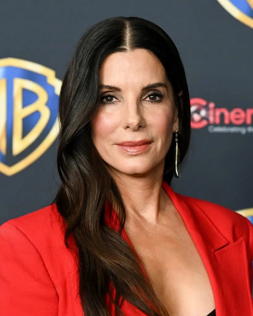 Sandra Bullock's two 'utterly totally different' kids, Louis and Laila, step into the highlight 3 Sandra Bullock in a red blazer, smiling at the camera.