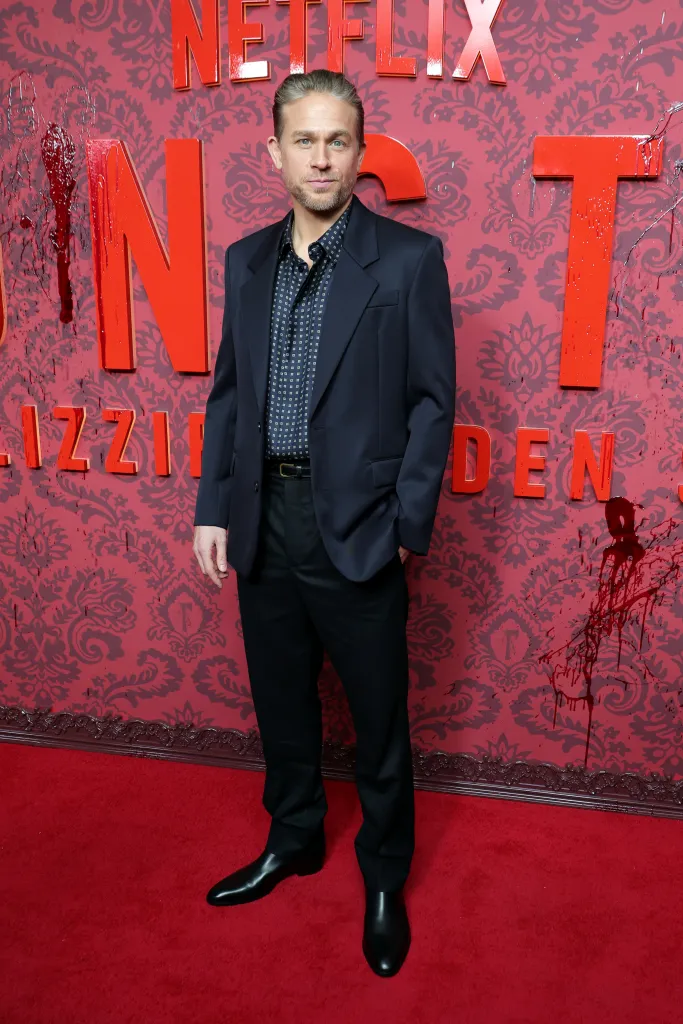 Charlie Hunnam poses on a red carpet in front of a red patterned set for Netflix "Monster: The Lizzie Borden Story" first.
