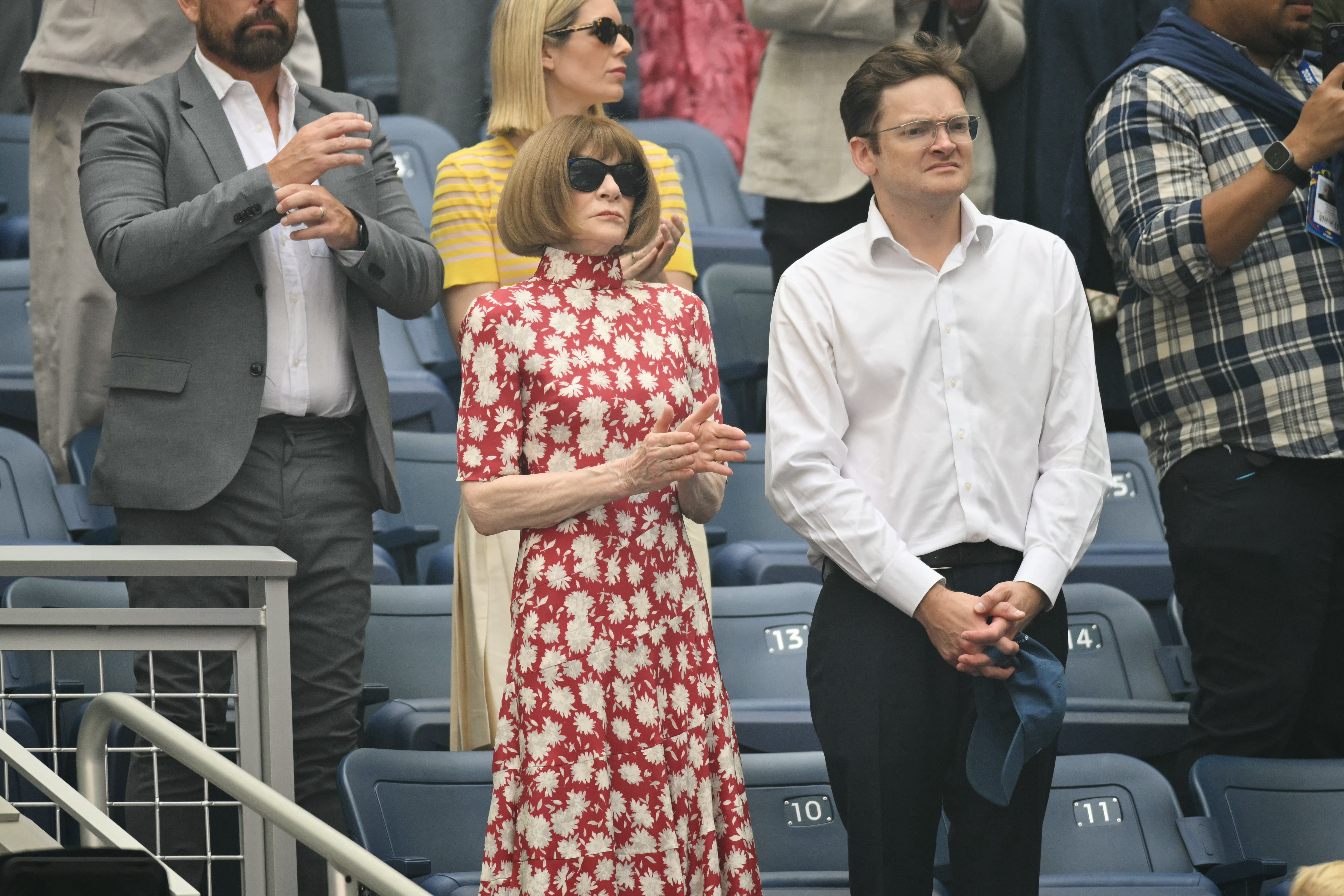 TENNIS-USA-OPEN Anna Wintour in a red floral dress, applauding, next to a man in a white shirt and glasses, during the US Open tennis tournament.