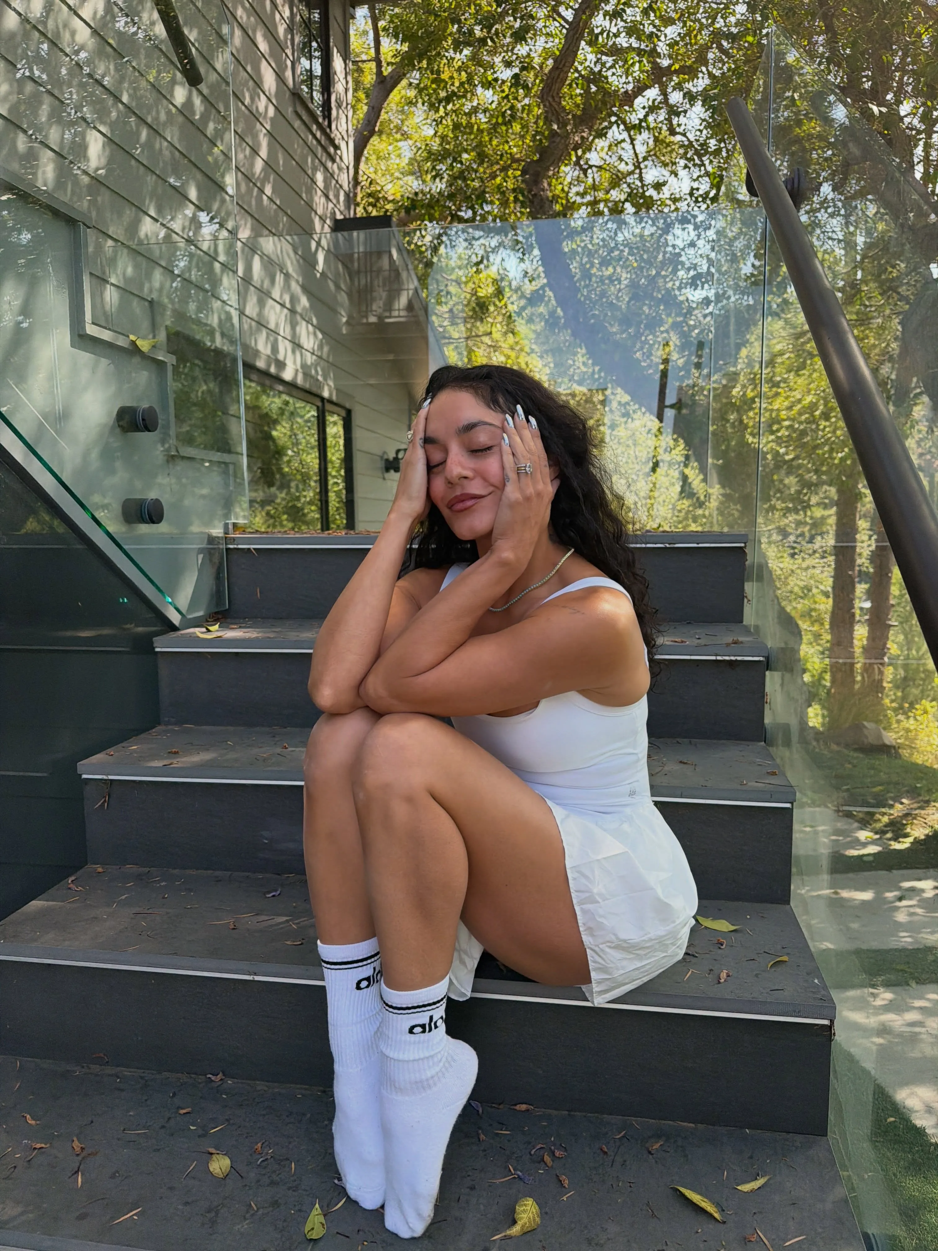 Vanessa Hudgens sitting on the steps, eyes closed and hands on her face.