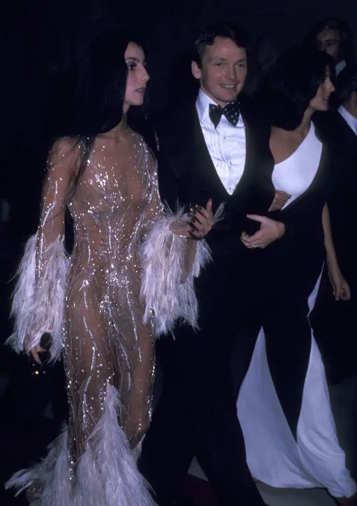 Cher wearing a long shimmering dress with feathers