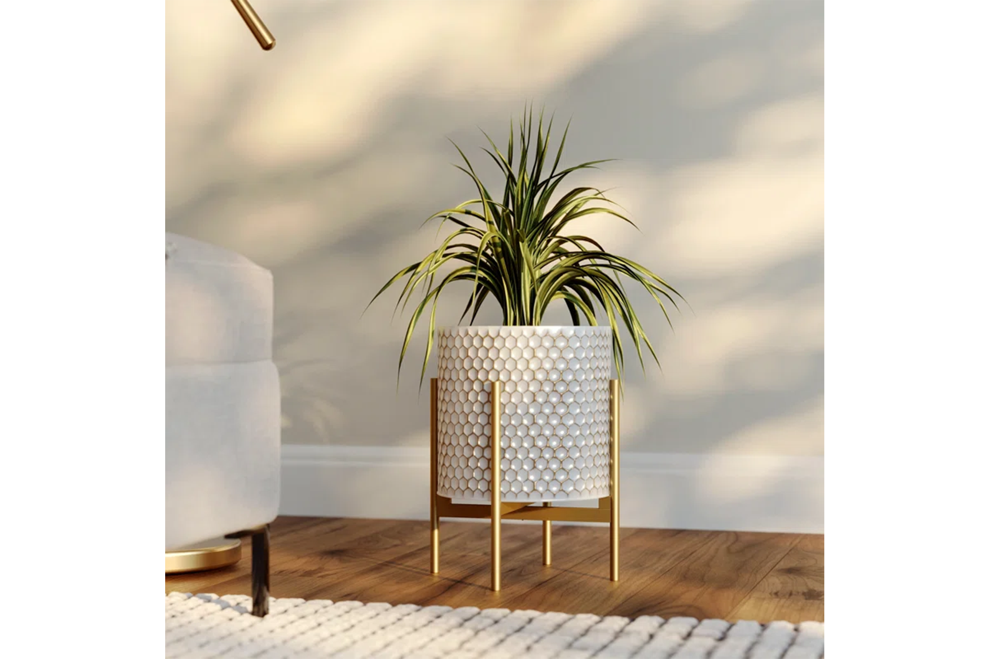 A plant in a white honeycomb-patterned planter with a gold stand sits on a wooden floor.